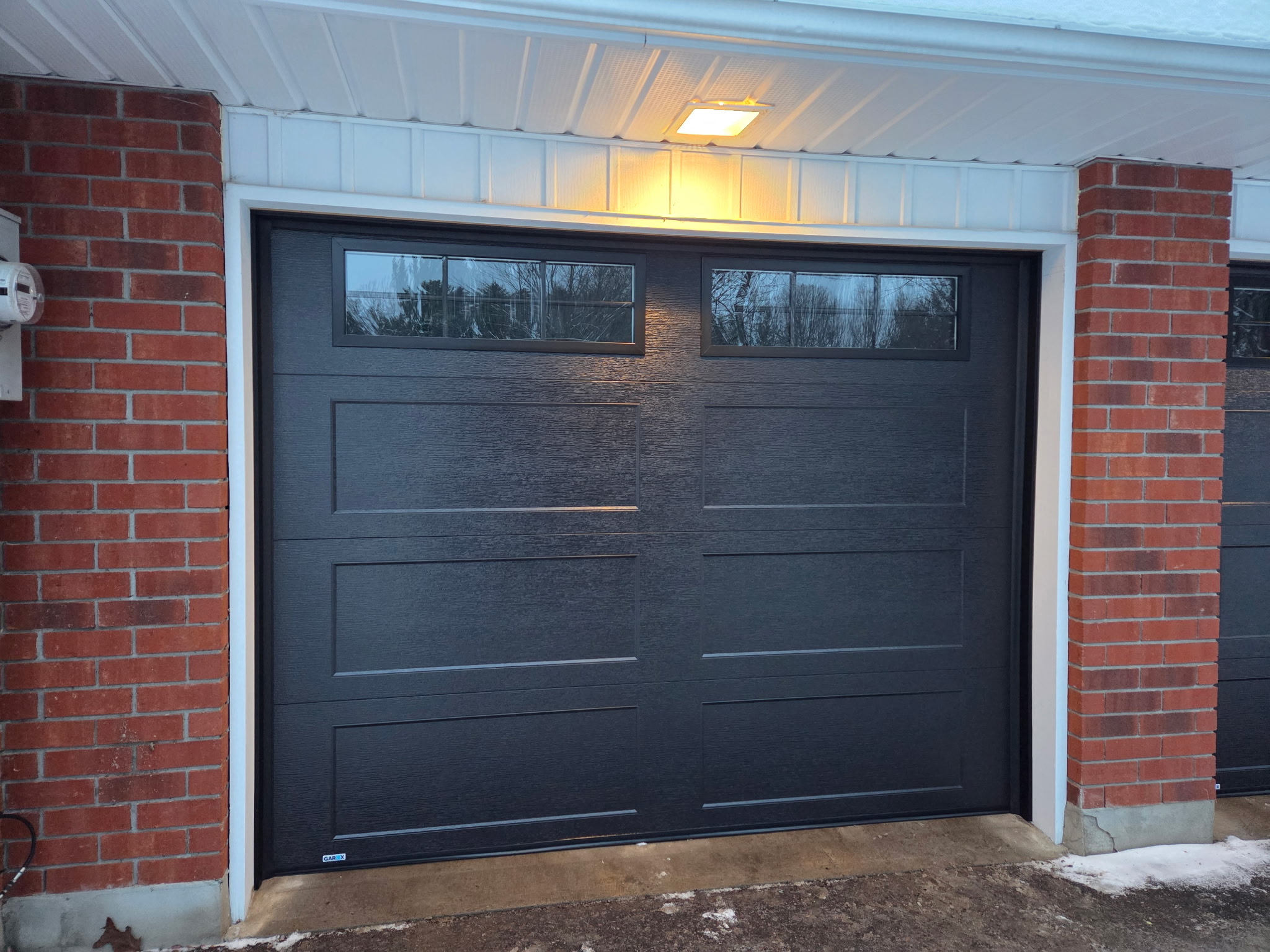 Dark charcoal garage door with windows on brick home by T&J Overhead Doors